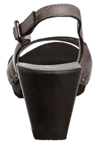 Sandale en cuir marron avec une fine bride de cheville, un talon en bois et une semelle texturée. Présente des clous en métal sur le côté et une semelle intérieure profilée.
