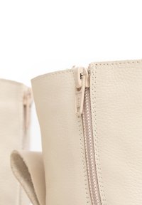 Stivaletti beige in pelle con zip laterale, texture liscia e cuciture a vista. La linguetta della zip presenta un discreto logo del marchio.