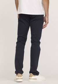 Pantalon bleu marine slim, en tissu mélangé avec du coton. Avec poches arrière et associé à des baskets beiges et blanches.