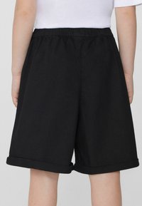 Černé bavlněné šortky s elastickým pasem, ohrnutým lemem a volným střihem, zobrazené z pohledu zezadu, bez viditelných kapes nebo detailů.