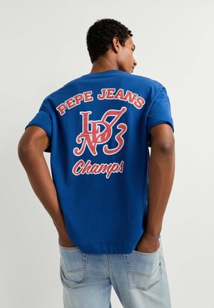 Hombre con una camiseta azul de Pepe Jeans con "PEPE JEANS", un estilizado "LD NO 3" y "Champs" impresos en rojo y blanco en la parte posterior.