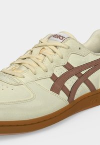 Κρεμ και καφέ παπούτσι Asics με δερμάτινο επάνω μέρος, ραμμένες λεπτομέρειες, επενδυμένο γιακά και σόλα από καουτσούκ.