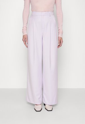 Person wearing high-waisted, wide-leg lavender trousers, pale pink long-sleeve top, and light pink square-toe shoes, standing against white background.
