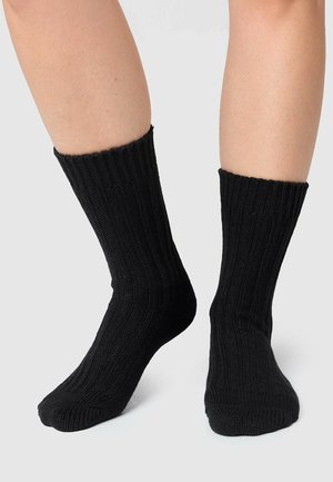 Chaussettes noires côtelées en matériau tricoté texturé, avec un haut bord et un bout arrondi. Aucun motif ni accent supplémentaire présent.