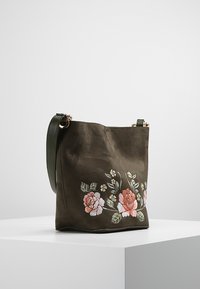 Sac seau en tissu vert avec broderie florale en rose et blanc, doté d'une seule bandoulière et de quincaillerie dorée.