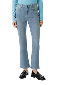 Jean en denim bleu clair avec une coupe droite, cinq poches et une fermeture à bouton, associés à des mocassins noirs. Taille plate avec des accents.