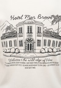 Σχέδιο κτιρίου του ξενοδοχείου Mar Bravo με φοίνικα και βουνά, συνοδευόμενο από ποιητικό κείμενο καλωσορίσματος για την άγρια πλευρά της Πάλμας.