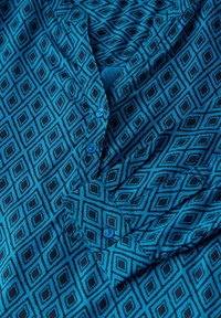 Chemise bleue boutonnée avec un motif en losange de bleu plus foncé. Le tissu a une texture lisse, avec un col et des boutons visibles.