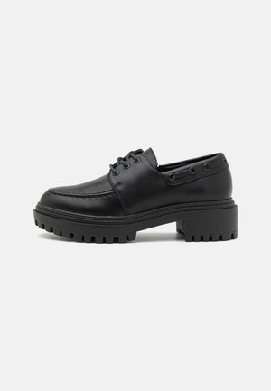 Black leather shoes with a rounded toe, lace-up design, and chunky rubber sole featuring textured grooves for traction.