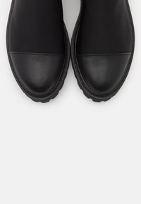 Czarne buty wsuwane z gładkim skórzanym noskiem i tekstylną cholewą, z grubą gumową podeszwą i minimalnymi detalami szwów.