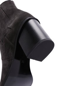 Botte de cheville en daim noir avec un talon bloc conséquent. L'empeigne présente des détails de coutures verticales pour plus de texture. Taille 36 marquée sur la semelle.