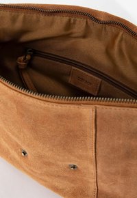 Intérieur d'un sac à main en daim tan, avec une poche zippée, un revêtement doux et des accents en métal. Coutures visibles et étiquette présentes.