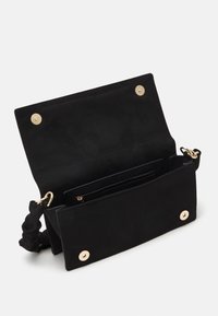 Czarna skórzana torebka z złotymi okuciami, zapięciem na klapę oraz teksturowanym wnętrzem z kieszonką na zamek. Dołączony pasek do noszenia na krzyż.