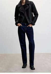 Czarna kurtka z sztucznej skóry z szarym futrzanym kołnierzem, w zestawieniu z ciemnoniebieskimi dżinsami i czarnymi botkami na kostkę. Gładka tekstura, dopasowany krój.
