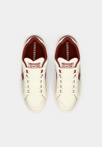 Off-white leather sneakers with red accents, perforated toe, flat laces, and Converse All Star branding on the tongue and sides.