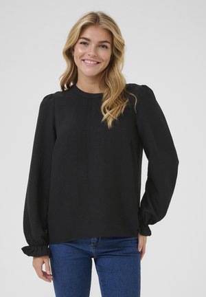 Svart blus med lång ärm, rund halsringning och puffärmar. Slät textur med gathered manschetter. Tillsammans med blå jeans.