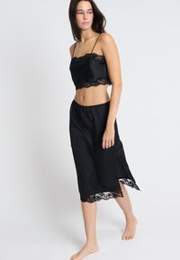 Czarny satynowy zestaw składający się z topu na ramiączkach z koronkowym wykończeniem i dopasowanej midi spódnicy z bocznymi rozcięciami oraz koronkowymi akcentami.