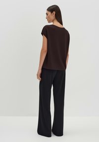 Top marrone a maniche corte con vestibilità rilassata, abbinato a pantaloni neri a gamba larga. L'outfit presenta texture morbide e lisce e un design semplice.
