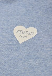 Tissu bleu clair avec un cœur blanc contenant les mots "STUDIO CLUB" imprimés en lettres majuscules.