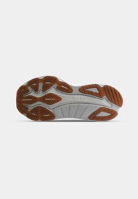 La semelle de la chaussure présente une base en caoutchouc gris avec une texture rainurée, renforcée par des sections marron en motif zigzag pour une meilleure traction.