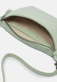 Mintgroene leren clutch met een ritssluiting, binnenvak en afneembare polsband. Zachte textuur en minimalistisch ontwerp.