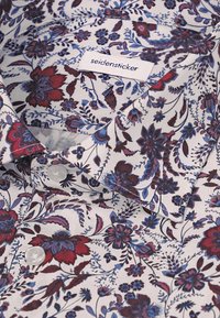 Chemise blanche avec un motif floral bleu et rouge et des boutons blancs, avec une étiquette de col indiquant "seidensticker."