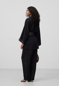 Zwart outfit met een losse, lange mouw top met satijnen accenten en wijde broekspijpen. Inclusief een textuur handtas en sandalen met hak.