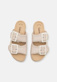 Beige nahkaliukkaat sandaalit, joissa on kaksi säädettävää solkea, pehmustettu pohja ja näkyvät tikit reunoilla. Tasapohjainen muotoilu.