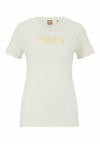 Camiseta de manga corta color crema con cuello redondo. Presenta un logo dorado brillante de "BOSS" en la parte frontal. Hecha de una tela suave y lisa.