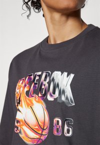 Camiseta de algodón negra con un gran gráfico colorido de un balón de baloncesto y "REEBOK 86" en texto metálico en la parte delantera.