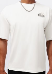 Weißes Kurzarm-T-Shirt mit einem runden Halsausschnitt, das ein Barcode-Graphic und den Text "YOURTURN" auf der linken Brustseite zeigt. Glatte Textur.