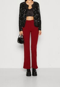 Svart kappa med paljetter över en svart satin crop top, parat med högmidjade bordeauxfärgade utsvängda byxor och svarta plattformsskor.