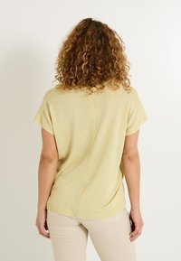 Haut en tricot à manches courtes, de couleur jaune clair, avec une coupe décontractée, une fermeture à boutons au dos et une texture douce. Le design comprend un ourlet arrondi.
