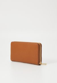 Portafoglio in pelle marrone con finitura testurizzata, dotato di una cerniera dorata e un tassello decorativo, di forma rettangolare. Design minimalista.