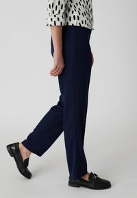 Marineblauwe gepaste broek van zacht materiaal met een rechte pijp, gecombineerd met zwarte instappers met een banddetail.