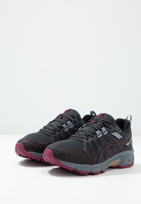 Chaussures de sport noires avec une tige en mesh texturé, des accents gris et des détails roses ; dotées d'une semelle rembourrée et d'un embout renforcé.