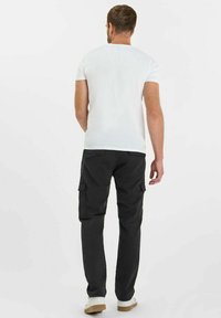Zwarte cargobroek met zijzakken, gedragen met een eenvoudig wit T-shirt en beige sneakers. De stof lijkt duurzaam met een gladde textuur.