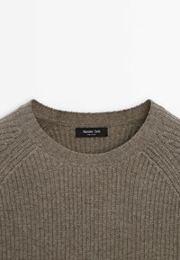Pull en maille côtelée marron avec col rond et étiquette noire visible au niveau du col portant l'inscription "Massimo Dutti Made in China."