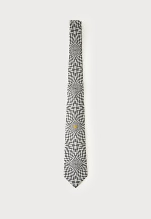 Cravate noire et blanche avec un motif géométrique en étoile et un petit emblème de lion doré près du bas.