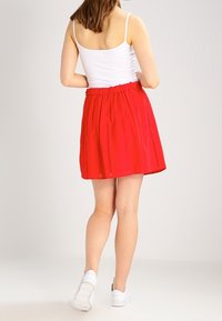Jupe rouge avec une taille élastique, présentant un design en couches et des détails en découpes œillets, associée à des baskets blanches.