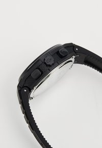 Black digital watch with a textured rubber strap, silver case back, and three buttons on the side for functionality.