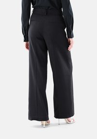 Schwarze weit geschnittene Hosen aus leichtem Stoff mit einem hoch geschnittenen Design und zwei Gesäßtaschen, die eine glatte Textur und eine minimalistische Gestaltung aufweisen.