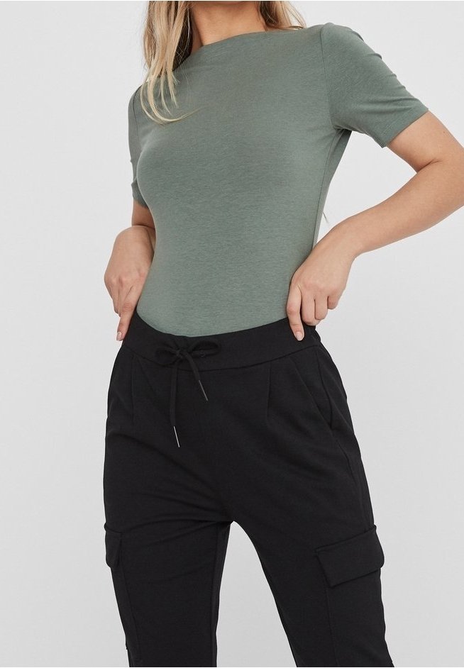 Femme portant un haut court moulant vert olive rentré dans un pantalon cargo noir à taille coulissante, debout les mains sur les hanches.