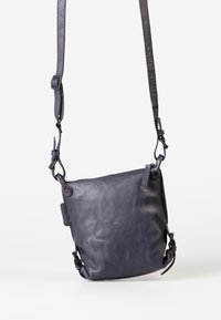 Borsa a tracolla in pelle viola con texture liscia, tracolla regolabile e dettagli in metallo. Chiusura con zip e discreto marchio.