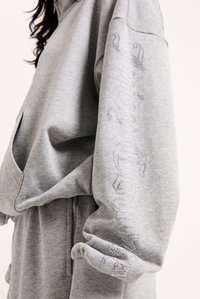 Γκρι φούτερ με μακριά μανίκια, που διαθέτει απαλή υφή και λεπτομέρειες με κρύσταλλα κατά μήκος του αριστερού μανικιού, σχεδιασμένο για χαλαρή εφαρμογή.