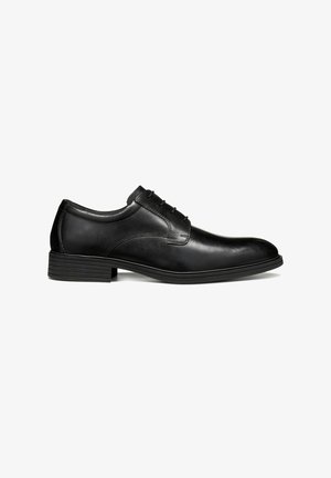 Chaussure habillée pour homme en cuir noir avec fermeture à lacets et petit talon empilé, vue de côté sur fond blanc.