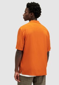 Camisa naranja de manga corta con una textura suave, un corte relajado y aberturas laterales. El cuello es plano con un diseño limpio.
