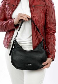Black leather handbag with a pebbled texture, crescent shape, and a functional shoulder strap. The hardware is subtle, featuring a silver logo.