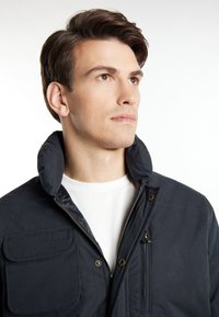 Marineblau isolierte Jacke mit hohem Kragen, Frontreißverschluss und mehreren Taschen; aus glattem Stoff mit sichtbaren Nähten.