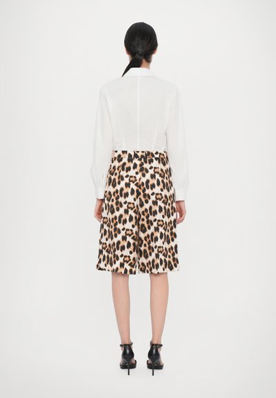 White long-sleeve shirt paired with leopard print shorts, featuring a beige base with black and brown spots, and black heeled sandals.